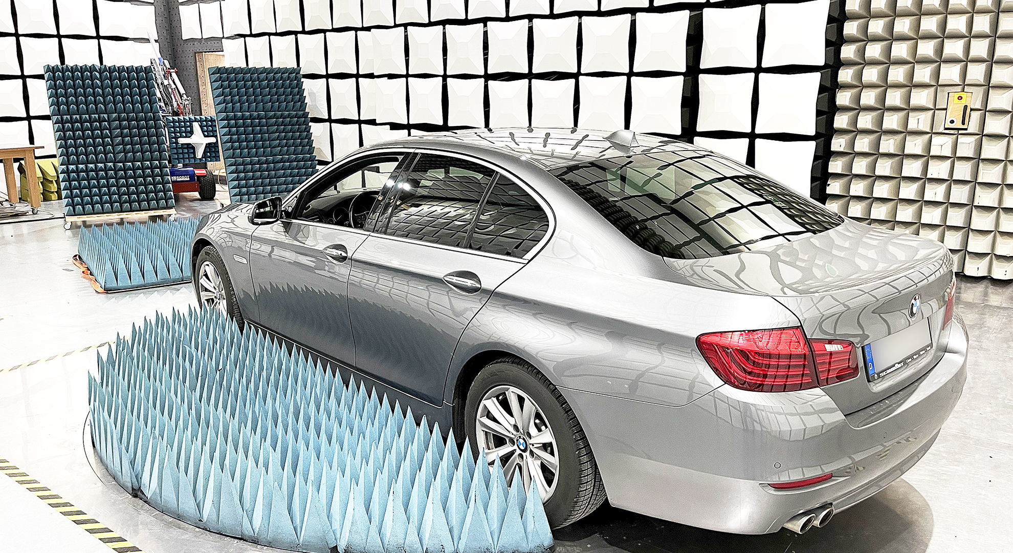 Ein glänzendes Auto der Marke BMW wird Abstrahlungsmessungen in einer Testhalle unterzogen. Dabei kommt unter anderem ein Antennen-Kran zum Einsatz.