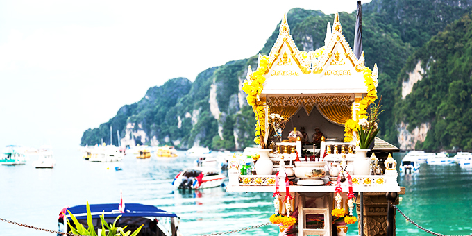 Traditional spirit house in Thailand (san phra phum) against turquoise sea water, ships and mountains.